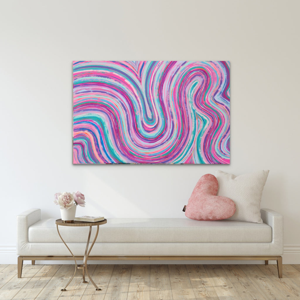 A colorful abstract canvas print with swirling pink, purple, blue, and teal lines, displayed on a white wall above a modern white sofa with a pink heart pillow in a styled living room setting.