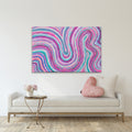 A colorful abstract canvas print with swirling pink, purple, blue, and teal lines, displayed on a white wall above a modern white sofa with a pink heart pillow in a styled living room setting.